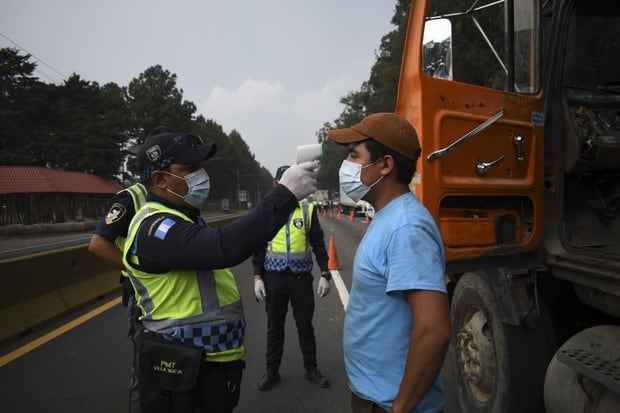Un oficial de policía de tránsito verifica la temperatura de un camionero como medida preventiva contra el nuevo coronavirus, durante un toque de queda parcial ordenado por el gobierno en Villa Nueva, Guatemala, el 2 de abril de 2020 (Foto: Johan Ordoñez / AFP)
