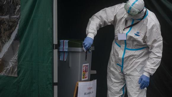 Un miembro del comité electoral que usa un equipo de protección desinfecta una boleta de votación el 6 de octubre de 2020 en Praga, antes de las elecciones generales en República Checa, en medio de la pandemia de coronavirus. (MICHAL CIZEK / AFP).