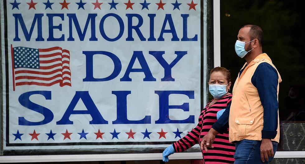 Las personas que llevan máscaras faciales pasan junto a un cartel que anuncia una venta de Memorial Day a medida que más empresas reabran en medio de la pandemia de coronavirus, en Arlington, Virginia. (Foto: AFP/Olivier DOULIERY)