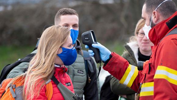 Un bombero verifica la temperatura de una mujer que lleva una máscara protectora debido al coronavirus en el cruce fronterizo entre Austria y Eslovaquia. (AFP / JOE KLAMAR).