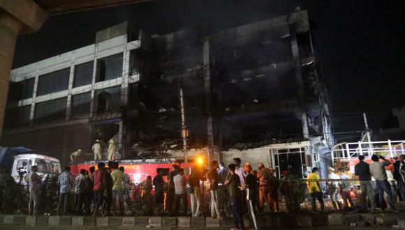 Los miembros del equipo de rescate y los espectadores se paran mientras los bomberos apagan un incendio que se desató en un edificio comercial en el suburbio occidental de Delhi.