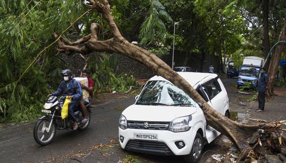 Un motociclista pasa junto a un automóvil aplastado por un árbol en una calle de Mumbai, India, después del paso del ciclón Tauktae. (Foto de Sujit JAISWAL / AFP).