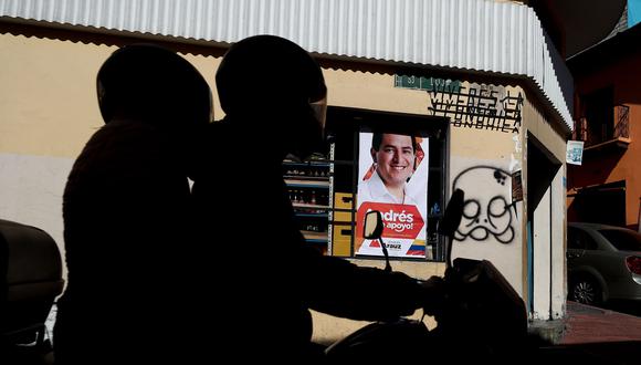 Dos personas cruzan en moto frente a un cartel del candidato Andrés Arauz. EFE