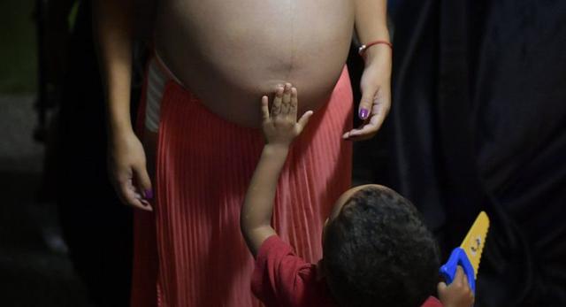 El sobrino de Ada Mendoza le toca el vientre de embarazada mientras está de pie en el departamento de sus padres donde vive con su pareja y siete familiares en el barrio Catia de Caracas, Venezuela. (Foto: AP /Matias Delacroix).