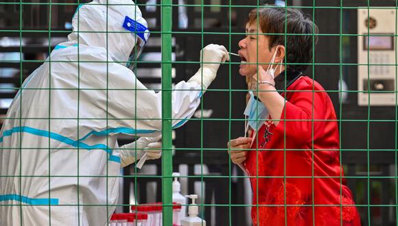Un trabajador de la salud toma una muestra de hisopo de una mujer en la entrada de un área residencial bajo bloqueo por coronavirus Covid-19 en Shanghai el 8 de junio de 2022. (Héctor RETAMAL / AFP).