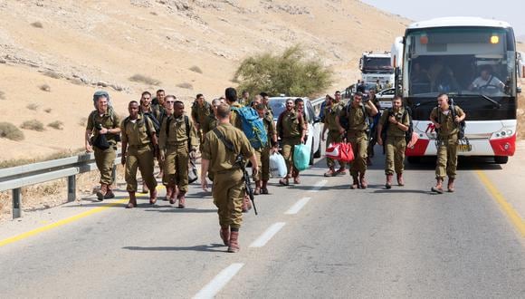 Soldados israelíes que llevan pertenencias caminan por una carretera cerca del sitio de un ataque a un autobús israelí, al este de la aldea de Tubas, en el norte de la Cisjordania ocupada, el 4 de septiembre de 2022. (Foto de AHMAD GHARABLI / AFP)