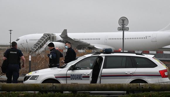 Los agentes de aduanas franceses se encuentran junto a un vehículo de aduanas con un Airbus A340 al fondo que estuvo parado en la pista desde el 21 de diciembre por sospecha de "tráfico de personas", en el aeropuerto de Vatry, al noreste de Francia, el 25 de diciembre de 2023. (Foto de FRANCOIS NASCIMBENI / AFP)