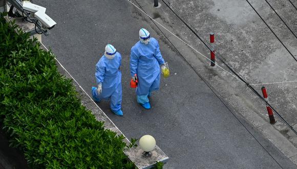 Trabajadores de la salud con equipo de protección personal (EPP) caminan por una calle después de salir de un vecindario durante el confinamiento por coronavirus Covid-19 en Shanghái el 16 de abril de 2022. (Héctor RETAMAL / AFP).