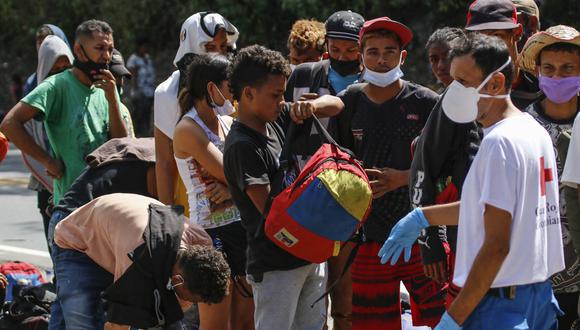 Migrantes venezolanos usan mascarillas mientras hacen cola para recibir alimentos y medicamentos de miembros de la Cruz Roja en una carretera en Cúcuta, Colombia, el 2 de febrero de 2021. (Foto referencial, Schneyder MENDOZA / AFP).