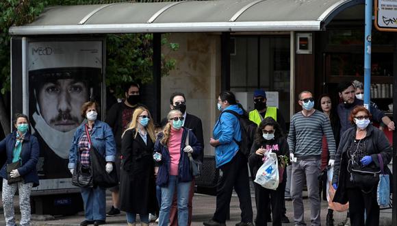 Las personas que usan máscara protectora esperan en una estación de autobuses en Atenas. (Photo by Louisa GOULIAMAKI / AFP)