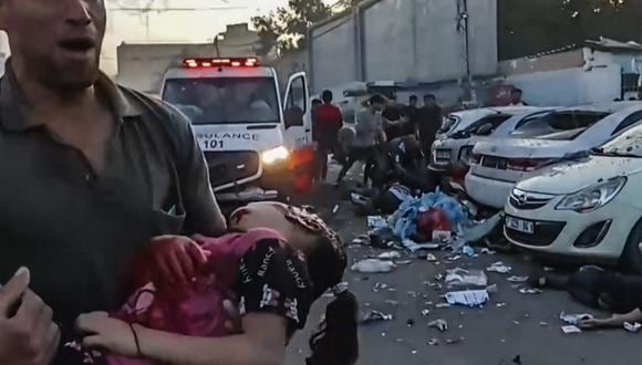 En esta imagen tomada de un video de AFPTV se muestra a un hombre cargando a una niña herida mientras corre cerca de una ambulancia dañada en un ataque israelí reportado frente al hospital Al-Shifa en la ciudad de Gaza el 3 de noviembre. (Foto de AFPTV STRINGER / varias fuentes / AFP)