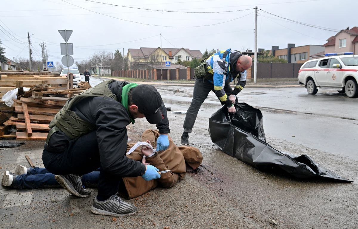 A community worker cuts the rope from the corpse of a man with his hands tied behind his back while another prepares a plastic bag to put him in in the city of Bucha, near kyiv, Ukraine, on April 3, 2022. (SERGEI SUPINSKY/ AFP).