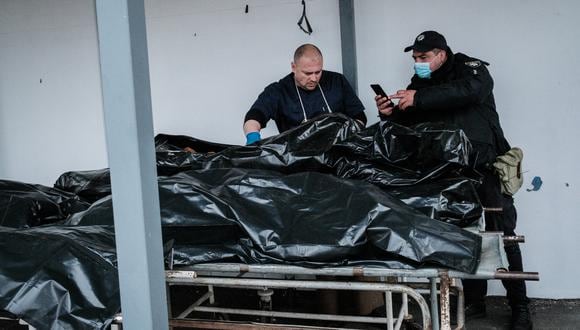 Un oficial de policía toma una foto de una víctima muerta colocada en una bolsa para cadáveres, en una morgue en Bucha, el 18 de abril de 2022, durante la invasión rusa de Ucrania. (Yasuyoshi CHIBA / AFP)