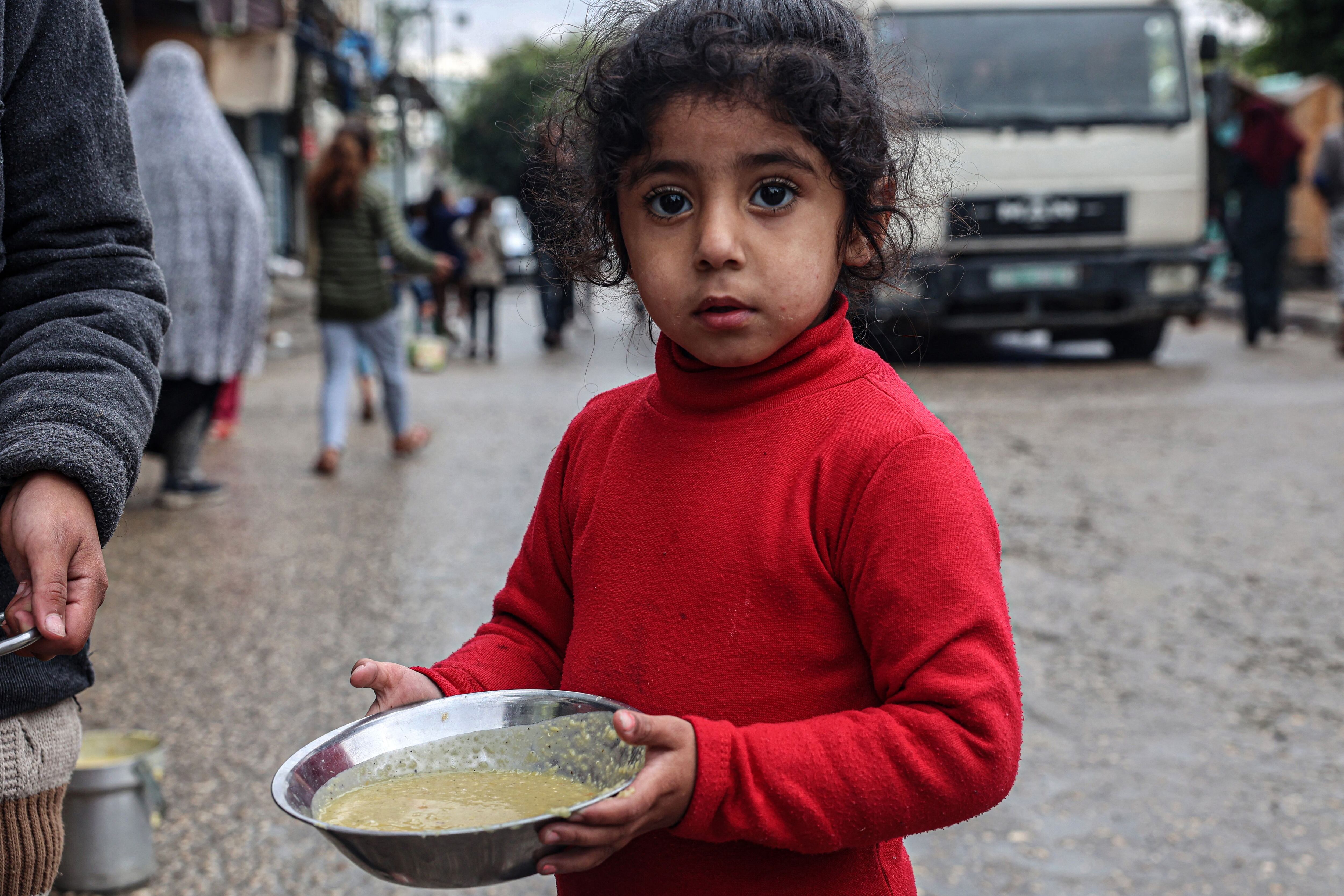 A displaced Palestinian girl carries a ration of lentil soup distributed by volunteers in Rafah, southern Gaza Strip, on February 18, 2024. (Photo by SAID KHATIB/AFP).