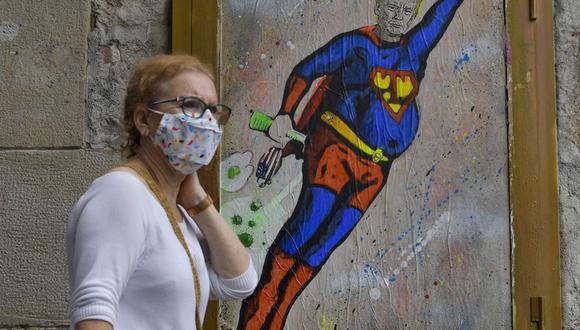 Una mujer pasa junto a una nueva obra de arte del artista callejero TVBoy que representa al presidente de Estados Unidos, Donald Trump, vestido con un disfraz de Superman y volando a través de las nubes COVID-19 en Barcelona el 8 de octubre de 2020 (Foto: Pau BARRENA / AFP).