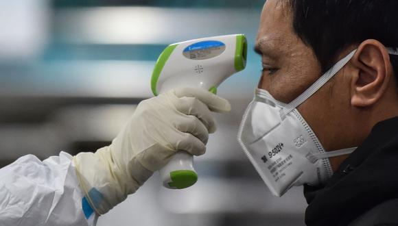 Un miembro del personal médico que usa ropa protectora toma la temperatura de un hombre en Wuhan, la ciudad de China donde se originó el coronavirus. (Foto de Hector RETAMAL / AFP).