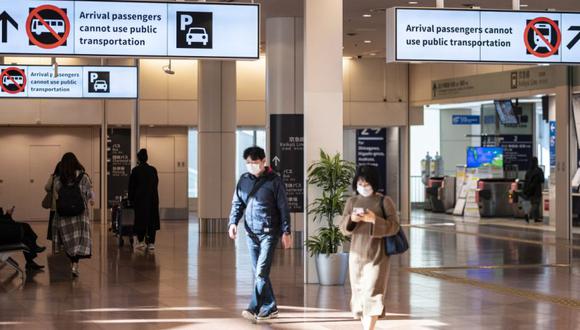 La gente camina debajo de los letreros para los pasajeros que llegan del extranjero en la sala de llegadas del aeropuerto de Haneda en Tokio el 8 de noviembre de 2021. (Foto: Charly TRIBALLEAU / AFP).