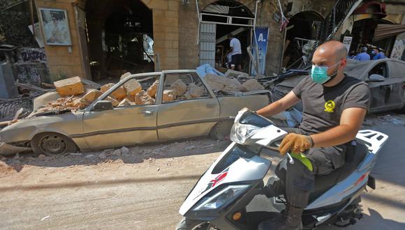Imagen referencial. Un hombre que llevaba una mascarilla contra el coronavirus conduce su motocicleta frente a autos y tiendas dañadas por la explosión en Beirut, Líbano. (AFP / STR).
