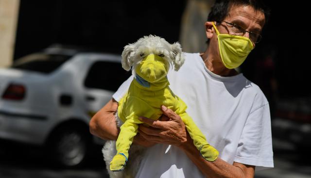 Un hombre lleva a su perro con un traje protector como medida preventiva contra la propagación del nuevo coronavirus. (AFP).