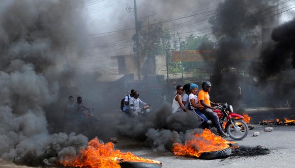 Los conductores de motocicletas pasan por un bloqueo de carretera en llamas mientras aumenta la ira por la escasez de combustible que se ha intensificado como resultado de la violencia de las pandillas, en Puerto Príncipe, Haití.