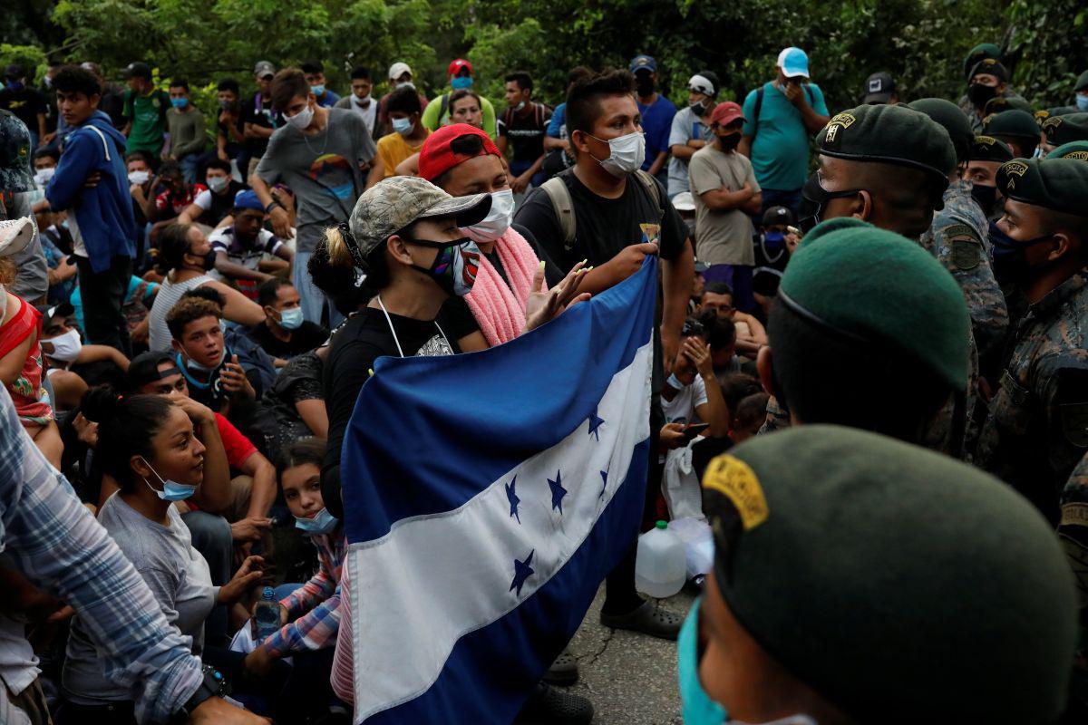 Los migrantes hondureños que intentan llegar a los EE.UU. sostienen una bandera hondureña mientras están parados frente a soldados guatemaltecos que bloquean una carretera para evitar que los migrantes lleguen a la frontera de México, en San Pedro Cadenas, Izabal, Guatemala. (REUTERS/Luis Echeverria).