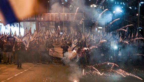 Fuegos artificiales estallan ante los manifestantes que marchan en una protesta contra la legislación de reforma judicial propuesta por el gobierno israelí en la ciudad central de Bnei Barak el 23 de marzo de 2023. (Foto de AHMAD GHARABLI / AFP)