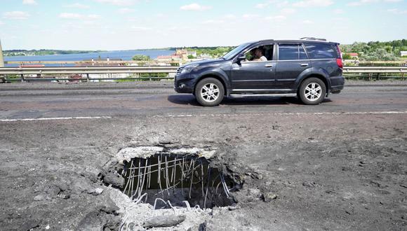 Un automóvil que pasa por un cráter en el puente Antonovsky (Antonivskiy) de Kherson que cruza el río Dnipro causado por un ataque con cohetes ucranianos, el 21 de julio de 2022. (Foto referencial de STRINGER / AFP)