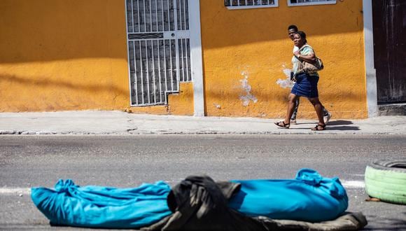 Dos personas caminan cerca de un cadáver de una persona en una calle de Petion-ville, en Puerto Príncipe, Haití, el 20 de marzo de 2024. (Foto de Mentor David Lorens / EFE)