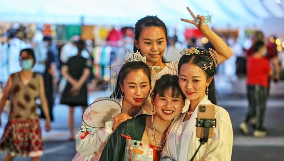 Esta foto tomada el 27 de agosto de 2020 muestra a mujeres con ropa tradicional tomándose un selfie mientras visitan un mercado nocturno en Wuhan, en la provincia central china de Hubei. (Foto de STR / AFP).