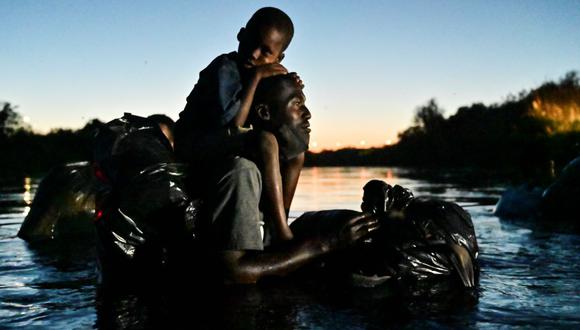 Un hombre carga a un niño sobre sus hombros mientras migrantes haitianos cruzan el río Grande entre Ciudad Acuña, estado de Coahuila, México, el 23 de septiembre de 2021. (PEDRO PARDO / AFP).