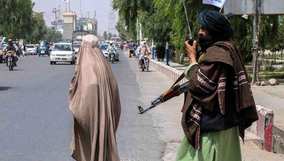 Un combatiente talibán patrulla Kandahar, Afganistán, el 19 de agosto de 2021, mientras pasa a su lado una mujer cubierta por la burka. (EFE / EPA / STRINGER).