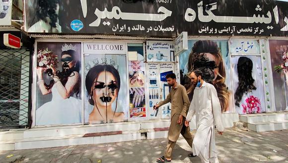 Dos hombres caminan junto a un salón de belleza cerrado y vandalizado en una calle de Kabul, Afganistán. (Foto: EFE)