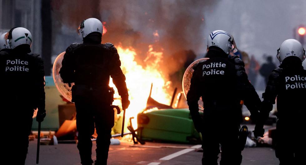 La policía antidisturbios de Bélgica pasa junto a contenedores en llamas mientras estallan enfrentamientos durante una manifestación contra las medidas del gobierno para frenar la propagación del coronavirus. (KENZO TRIBOUILLARD / AFP).