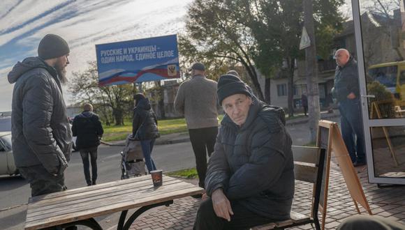 El hombre bebe su café con una cartelera del período de ocupación rusa "Los rusos y los ucranianos son un pueblo, un todo" en el fondo mientras la gente regresa a su vida cotidiana en el Kherson recién liberado el 14 de noviembre de 2022, en medio de la invasión rusa de Ucrania (Foto: BULENT KILIC / AFP)