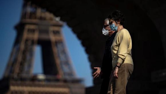 Dos peatones que usan mascarillas protectoras contra el coronavirus disfrutan del cálido clima primaveral mientras cruzan el puente Bir Hakeim, cerca de la Torre Eiffel, en París, Francia. (EFE / EPA / IAN LANGSDON).