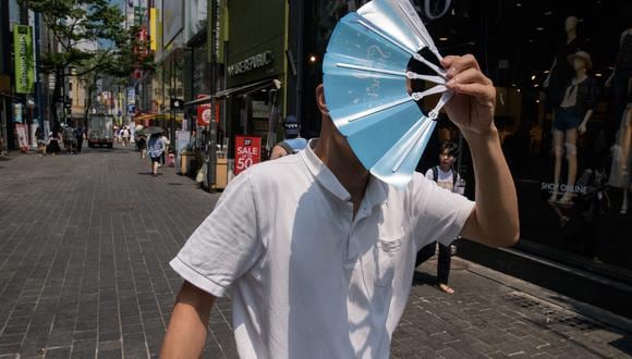 Imagen de archivo | Un hombre se protege la cara del sol mientras camina por el distrito comercial de Myeongdong en Seúl. (Foto de Ed JONES / AFP)
