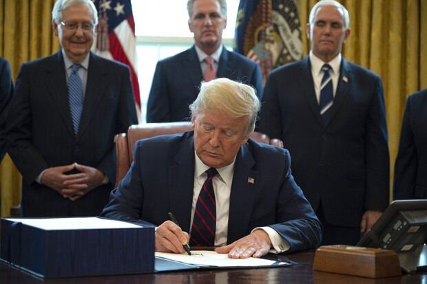 El presidente Donald Trump firma la ley CARES, un paquete de rescate de US$ 2 billones para proporcionar ayuda económica en medio del brote de coronavirus, en la Oficina Oval de la Casa Blanca (Foto: AFP)