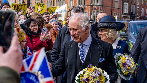 Imagen de archivo | El rey Carlos III de Gran Bretaña (centro) y Camilla, la reina consorte (derecha) de Gran Bretaña hablan con los simpatizantes después de asistir al Royal Maudy Service, donde el rey distribuye el dinero de Maundy a 74 hombres y 74 mujeres, reflejando la edad del monarca, en York Minster, norte de Inglaterra, el 6 de abril de 2023. (Foto de Charlotte Graham/PISCINA/AFP)