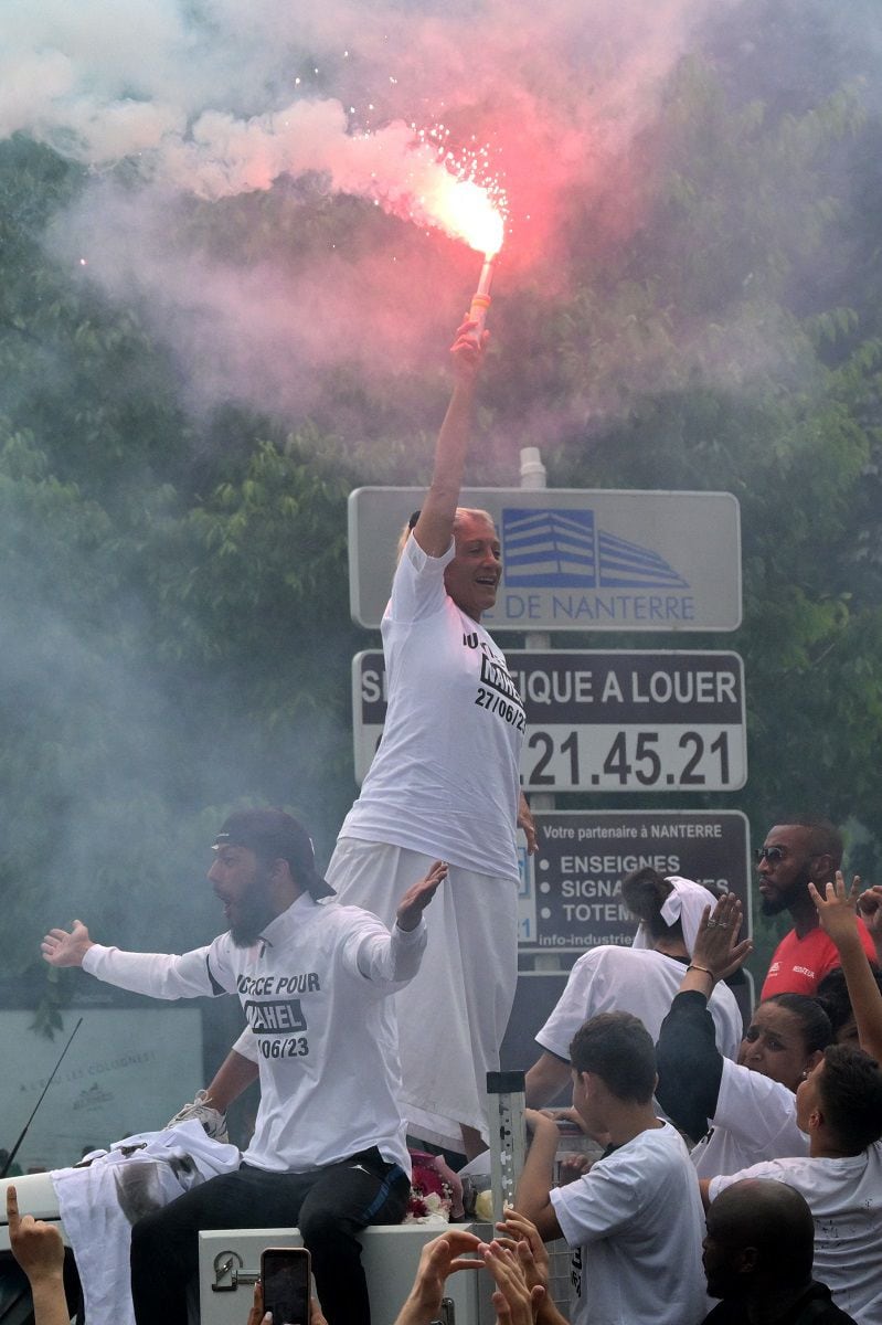 Mounia, the mother of Nahel, a teenager shot to death by a police officer, waves a sparkler as she stands on top of a truck during a march in commemoration of her son, in Nanterre, on June 29, 2023. (Photo by Alain JOCARD / AFP)