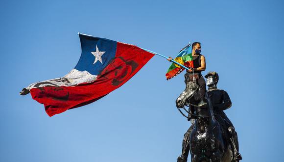 Un manifestante agita una bandera indígena chilena y otra mapuche desde lo alto del monumento General Baquedano en la Plaza Italia durante una protesta contra el gobierno del presidente chileno Sebastián Piñera el 9 de octubre de 2020 (Foto de Martín BERNETTI / AFP).