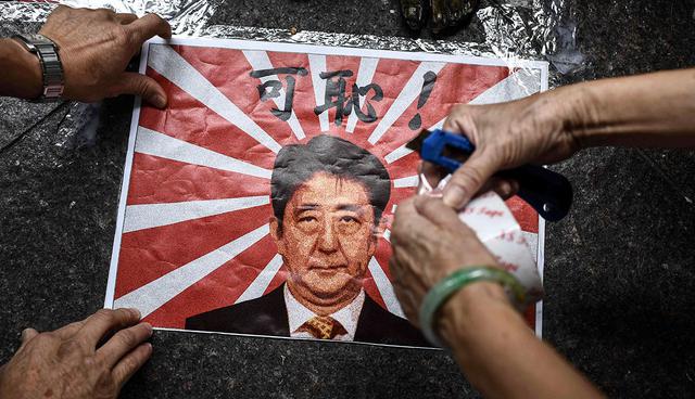 TOPSHOT - A poster depicting Japan's Prime Minister Shinzo Abe and the Japanese wartime imperial flag is taped next to the feet (top) of a "comfort woman" statue before a protest to mark the 86th anniversary of the 'Mukden Incident' in Hong Kong on September 18, 2017.  

 The 'Mukden Incident' took place in 1931, when Japanese soldiers blew up a railway in Manchuria as a pretext to take control of the entire northeastern region a few years before the outbreak of World War II.    / AFP / Anthony WALLACE
