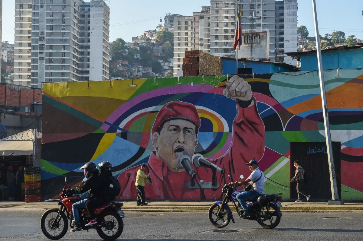 Men on motorcycles pass in front of a mural depicting the late President of Venezuela Hugo Chávez (1954-2013) in Caracas, Venezuela, on March 2, 2023. (Photo by Miguel ZAMBRANO/AFP)