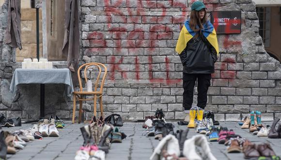 La diseñadora ucraniana Margarita Chala envuelta en una bandera ucraniana junto a varios zapatos, en la Plaza de la Ciudad Vieja de Praga, República Checa, el 15 de enero de 2023. (Foto referencial de Michal Cizek / AFP)