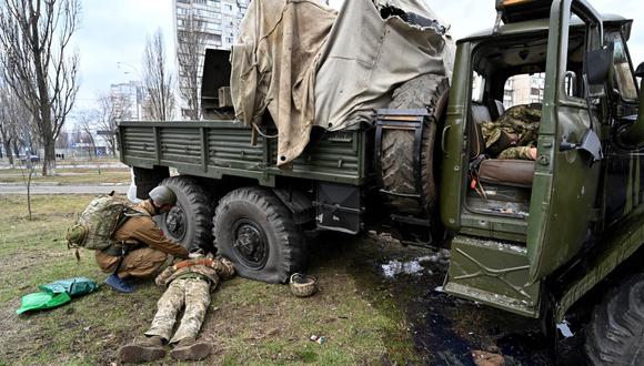 Un médico militar de Ucrania examina el cuerpo de un militar ruso que vestía un uniforme de servicio ucraniano y que yace junto a un vehículo después de que él y los miembros de un grupo de asalto recibieron disparos en Kiev el 25 de febrero de 2022. (SERGEI SUPINSKY / AFP).
