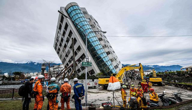 TOPSHOT - Japanese (L) and Taiwanese rescue workers (R) look at the Yun Tsui building (C), which is leaning at a precarious angle, in the Taiwanese city of Hualien on February 9, 2018, after the city was hit by a 6.4-magnitude quake late on February 6. Taiwan began demolishing three dangerously damaged buildings on February 9 as rescue workers combed the rubble of a hotel in a last-ditch effort to find seven people still missing after a deadly earthquake. / AFP / Anthony WALLACE