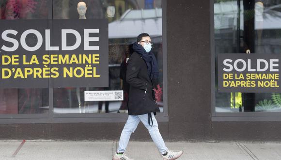 Un hombre usa una mascarilla mientras camina junto a los escaparates de las tiendas anunciando publicidad después de las rebajas de Navidad en el Boxing Day en Montreal. (Graham Hughes / The Canadian Press vía AP)