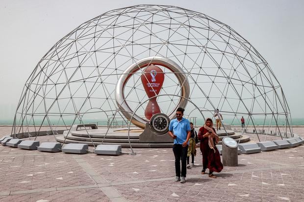 People pose for photos and walk away after seeing the installation of the clock marking the days until the start of the Qatar 2022 FIFA World Cup, along the waterfront in Qatar's capital Doha during a heavy storm of dust on May 17, 2022 as the horizon behind darkens in haze.  (Photo by KARIM JAAFAR / AFP)