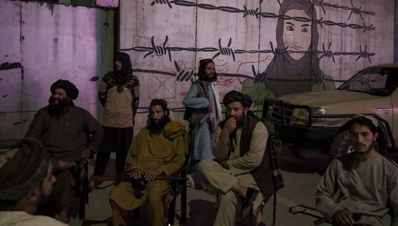 Miembros talibanes sentados frente a un mural que representa a una mujer detrás de un alambre de púas en Kabul, Afganistán, el martes 21 de septiembre de 2021. (AP Foto/Felipe Dana).