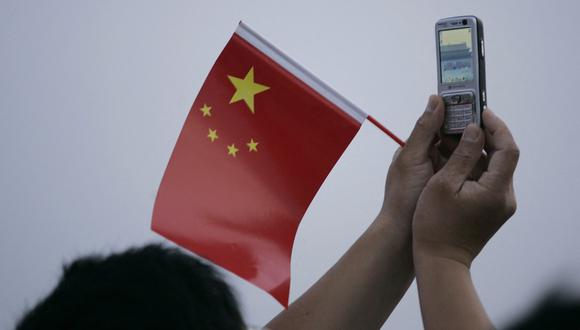 Un visitante toma una fotografía con su teléfono móvil al amanecer de la ceremonia de izamiento de la bandera en la plaza de Tiananmen en Beijing el 4 de junio de 2007. (Foto referencial de Peter PARKS / AFP)
