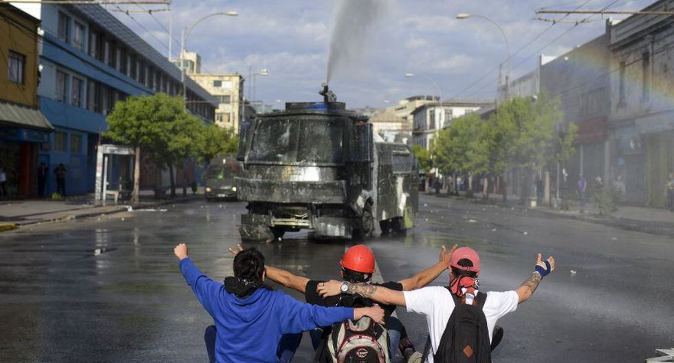 Anti-government protesters sit in front of a police water cannon in Valparaiso, Chile, Friday, Oct. 25, 2019. A new round of clashes broke out Friday as demonstrators returned to the streets, dissatisfied with economic concessions announced by the government in a bid to curb a week of deadly violence.(AP Photo/Matias Delacroix)